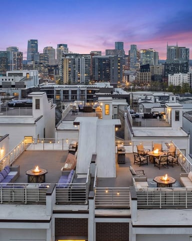 Rooftop terrace with fire pits and seating overlooking downtown city skyline at dusk