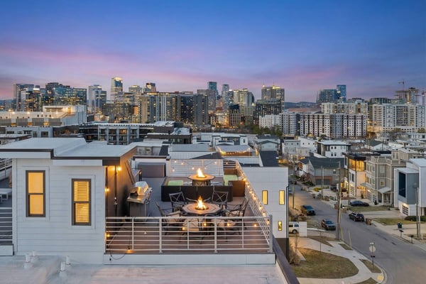 Modern rooftop deck with fire pit and city skyline at dusk, illuminated windows and downtown buildings in background