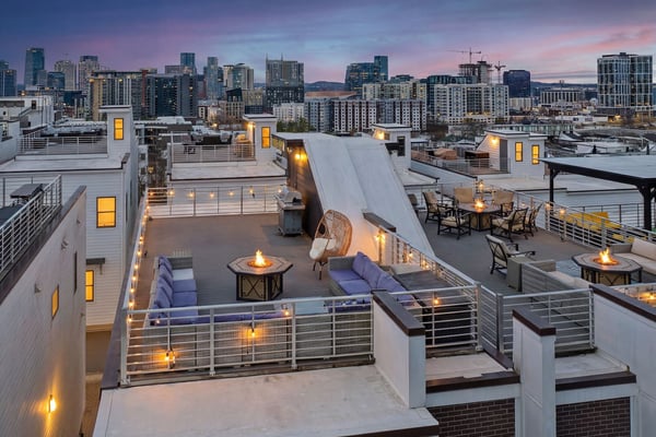 Rooftop terrace with fire pits, seating, and city skyline at dusk