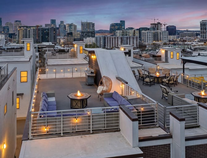 Rooftop terrace with fire pits, seating, and city skyline at dusk